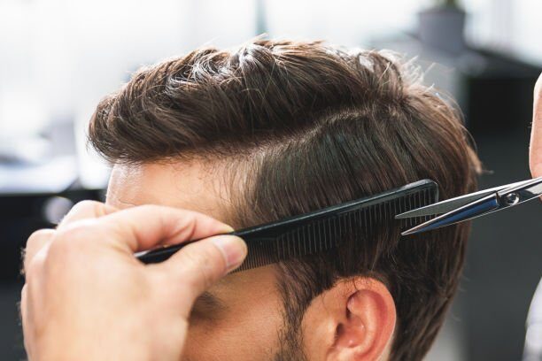 Close up of hairdresser arms cutting and combing male hair